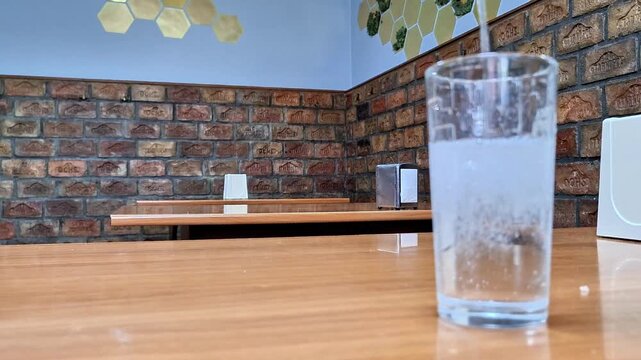 A clear glass of sparkling water stands on a wooden table in a cozy cafe with rustic brick walls. Refreshing bubbles rise through the water, creating a calm, inviting indoor dining atmosphere
