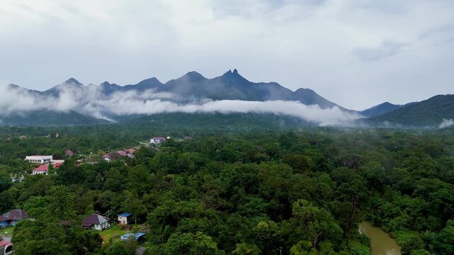Aerial footage of Mount Daik in Lingga, Indonesia, featuring low clouds drifting across the mountain slopes above dense tropical rainforest