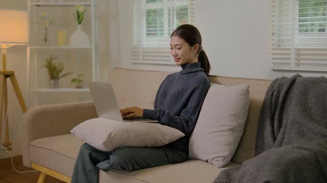 Woman sits comfortably on couch in cozy living room while using laptop