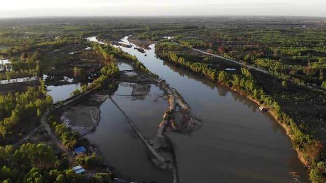 Aerial view of tropical river delta at sunset. Sunlight reflects in calm waters of river. Green forest and trees surround the watercourse at beautiful evening.