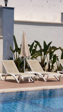 Luxury outdoor swimming pool with empty sun loungers, umbrellas and cascading water feature at a modern hotel resort. Summer vacation, relaxation, wellness and premium travel destination.