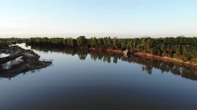 Aerial view of tropical river delta at sunset. Sunlight reflects in calm waters of river. Green forest and trees surround the watercourse at beautiful evening.