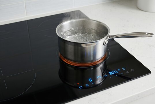 Close up of black induction cooktop with boiling water and blue lights