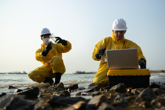 scientist in yellow hazmat suit collecting water sample for pollution analysis. researcher works on laptop, examining data on contaminated coastline