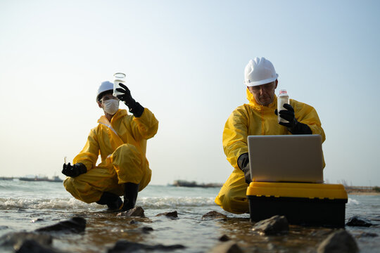 Two focused scientist in yellow protective suit working on water sample analysis. biologist and ecologist researching environmental pollution and contamination outdoors