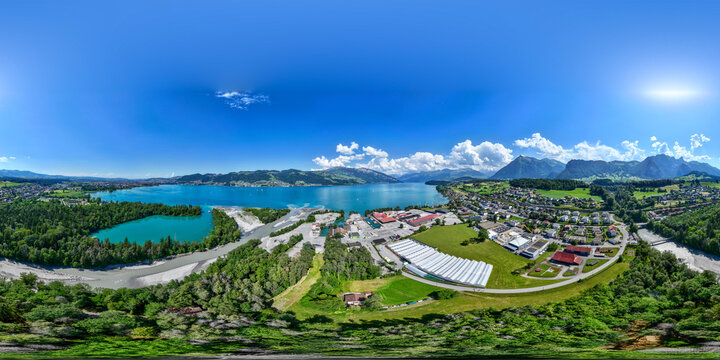 Aerial view of Lake Thun with its turquoise waters, surrounding green hills, industrial facilities, and residential houses in Spiez, Canton of Bern, Switzerland.