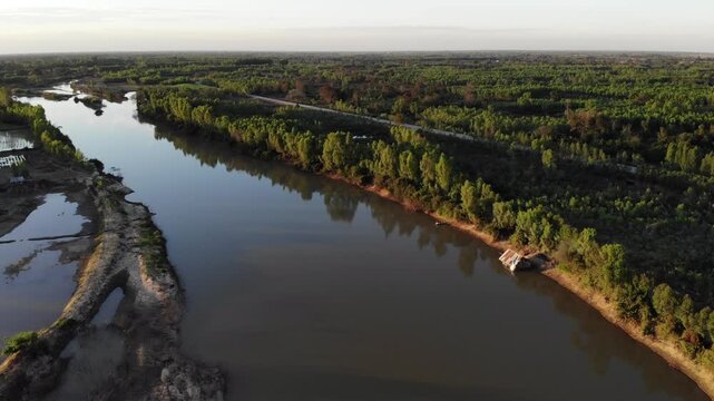 Aerial view of tropical river delta at sunset. Sunlight reflects in calm waters of river. Green forest and trees surround the watercourse at beautiful evening.