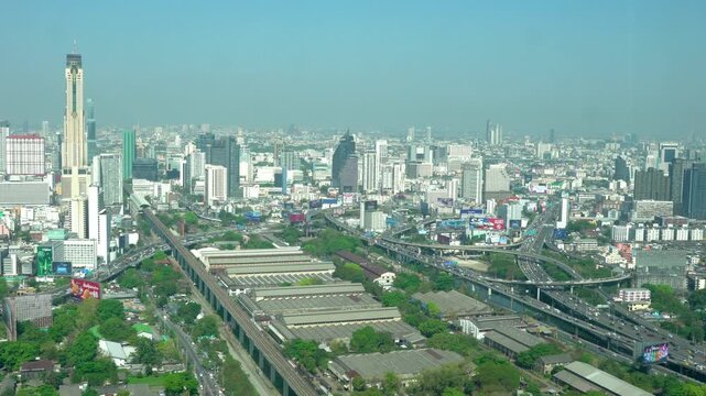 Static aerial view of the city skyline with elevated rail lines, highway interchanges, and dense urban development under a hazy sky.