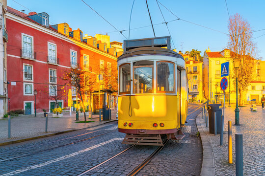 A traditional yellow vintage tram ascends a steep, narrow cobblestone street lined with historic buildings in Lisbon