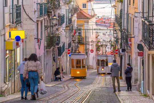 A classic yellow funicular tram ascending a steep, narrow cobblestone street lined with traditional colorful buildings  in Lisbon