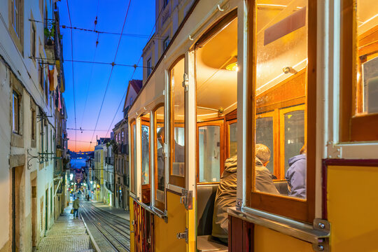 A classic yellow funicular tram ascending a steep, narrow cobblestone street lined with traditional colorful buildings  in Lisbon