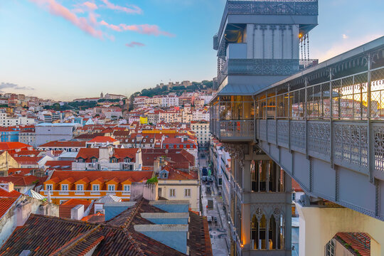 Panoramic city view featuring a historic iron lift structure and walkway overlooking traditional red roofed buildings and a distant hilltop castle  in Lisbon