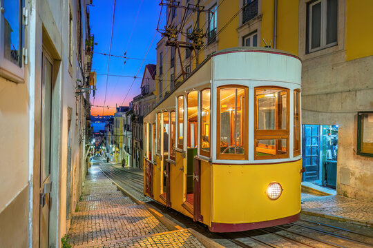 A classic yellow funicular tram ascending a steep, narrow cobblestone street lined with traditional colorful buildings  in Lisbon