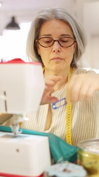 Mature female tailor sewing clothes in workshop