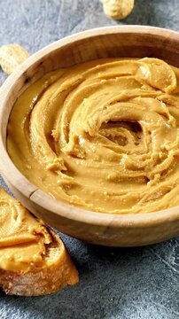 Creamy Peanut Butter in Wooden Bowl with Spread Toast Slice and Whole Peanuts Macro