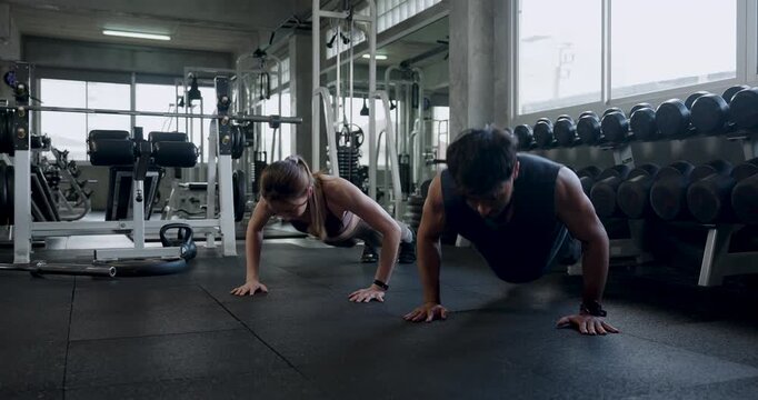 Young Asian couple completes push up workout together on modern gym floor, then kneels and smiles during recovery break, sharing support, motivation, wellness, healthy relationship teamwork routine