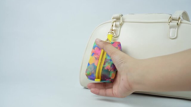 Minimal product video featuring a mini zipper keychain pouch attached to a handbag on a white background. A hand gently touches the hanging pouch to demonstrate its use as a decorative and functional 