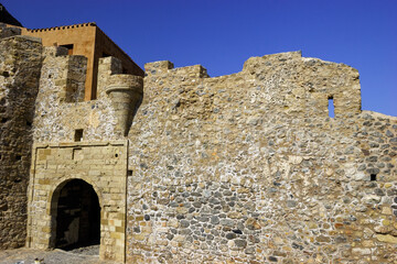 A stone archway and wall of a fortress under a clear blue sky. © Nick