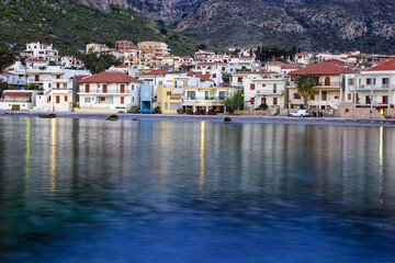 Fototapeta premium A coastal village with white buildings and red roofs sits on a hillside overlooking the sea, with reflections of the buildings visible in the water.