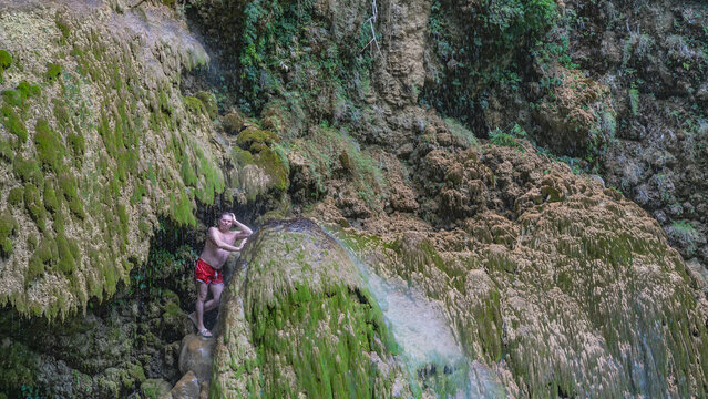 Exotic tropical waterfall. The water flows down the mossy terraces. A man stands on a ledge, under the drops, leaning on his elbow, squinting. Philippines. Cebu. Tumalog Falls.
