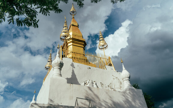 Low angle view of the golden That Chomsi Stupa on Mount Phousi under a dramatic sky, Luang Prabang, Laos