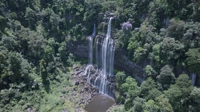 A drone flying over a waterfall in a deep green forest provides an aerial, top-down view of a National Park in Laos PDR.