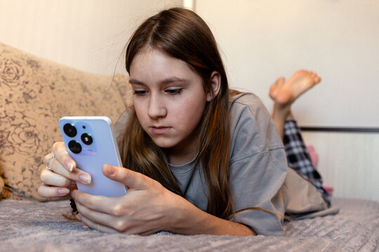 Girl lying on sofa with smartphone in hands, attentively looking on screen.