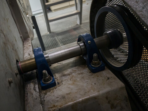 Industrial photo of rotating shaft with pulley, pillow block bearings, and belt guard in high-speed motion. Perfect for engineering, machine, and technical design themes.
