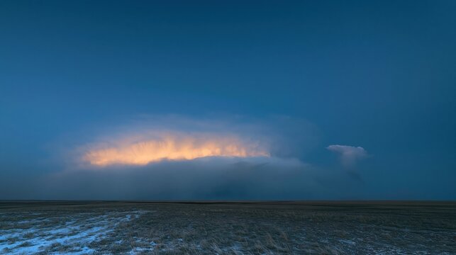 Storm cloud formation glowing with warm light over a dark prairie landscape, providing vast blue copy space for weather and climate concepts