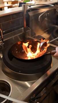 Chef stir-frying ingredients in a seasoned wok pan with fire flames. Cooking asian cuisine in a restaurant. Asian restaurant kitchen. Cinematic b roll of frying meat in a wok pan.
