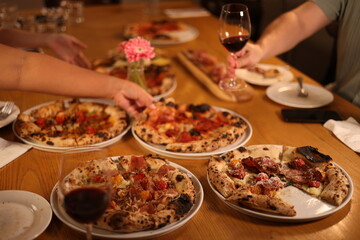 Obraz premium Friends Sharing Neapolitan Pizzas and Red Wine at a Restaurant Table