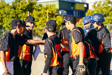 Obraz premium Coach and youth baseball team huddling together discussing strategy and building teamwork before a game