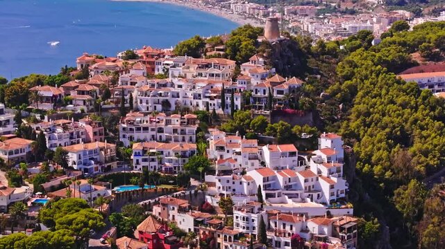 Drone footage of Almu&ntilde;&eacute;car, Granada, gliding toward white hillside villas above the bay, with a telephoto coastal compression and bright summer haze in southern Spain