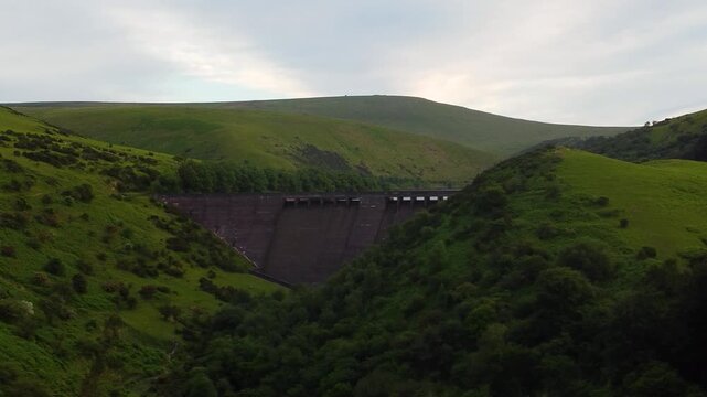 Meldon Dam spans a narrow Dartmoor valley as the drone glides toward the concrete wall between bright hillside slopes.