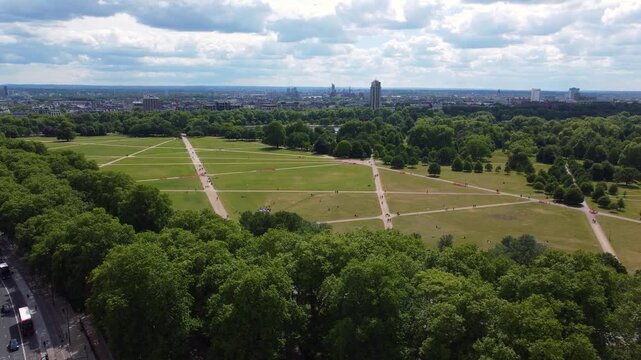 Aerial drone shot slowly revealing the vast green expanse of Hyde Park in London, UK. People relaxing on the grass with the city skyline