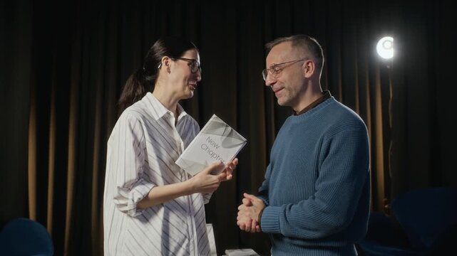 Portrait of middle aged Caucasian man presenting book to adult woman, then both looking at camera. Footage is ideal for book publishing promotions or educational marketing, zoom out