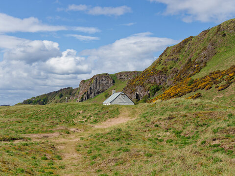 Looking down the Path along the grass covered dunes of St Cyrus Nature Reserve at the white painted Salmon Bothy in front of the Cliffs.