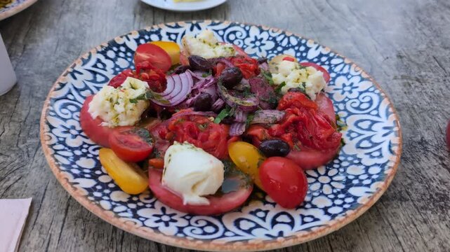 Cinematic close-up of a fresh tomato and burrata cheese salad on a restaurant table at an outdoor patio during a warm dusk evening