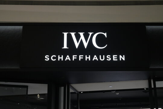 A bright IWC Schaffhausen logo sign glows above a luxury store entrance.