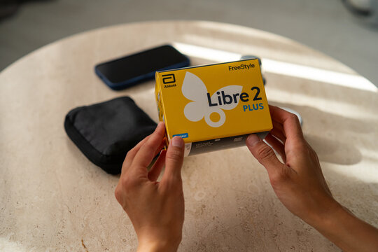 Minsk, Belarus - June 23, 2026: Cropped shot of human hands holding a FreeStyle Libre 2 Plus glucose sensor box over a table