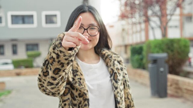 Woman points finger forward wearing leopard print coat and glasses on a street, smiling and engaging with camera; friendly confidence.