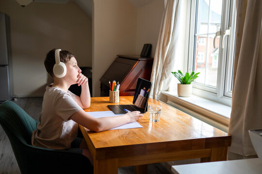 Schoolboy studying online while sitting at desk near window at home