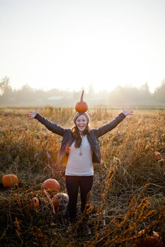 Joyful woman balances a pumpkin on her head in a patch