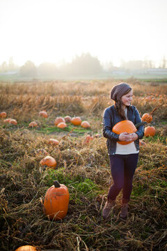 Smiling woman holds a pumpkin in a sunny patch