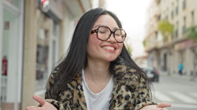 Woman wearing glasses and leopard coat with open hands blowing a kiss on a street; joy playfulness confidence.