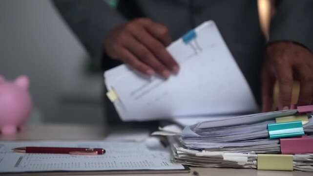 Professional close-up video of an employee sorting office paperwork and reviewing business files on a desk. Suitable for corporate administration, document organization, filing systems, productivity, 