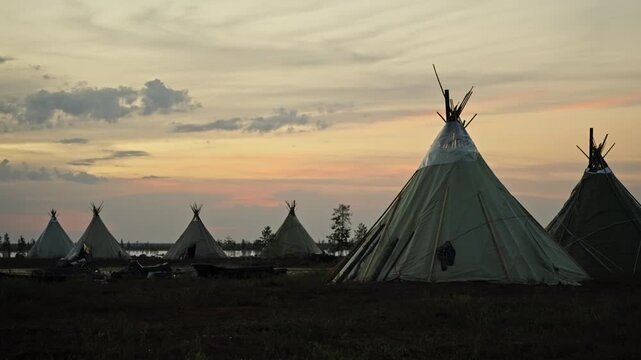 Traditional conical tents on tundra by a lake at sunset