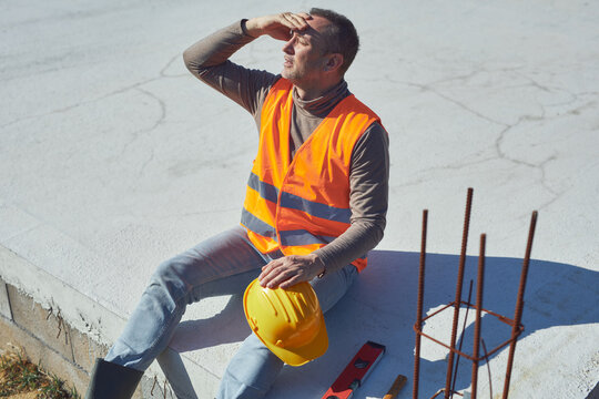 Construction worker having a heatstroke on a hot sunny day, headache, issues on a construction site outdoors.