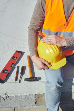 Construction worker working outdoors on a construction site, making a pause and holding a yellow hardhat.