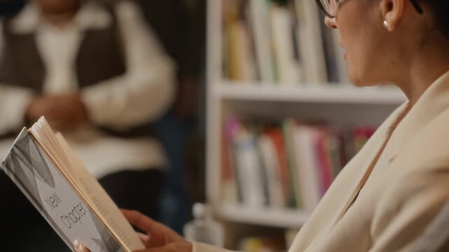 Tilt up shot of Caucasian woman holding book titled New Chapter and speaking during presentation in library. Footage is ideal for promoting book launches, literary events, or motivational seminars
